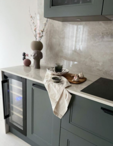 Närbild på kök med grågrön klassisk ramlucka som kombinerats med bänkskiva och stänkskydd i keramisksten dekton arga. Svarta detaljer och handtag. Även vinkyl.