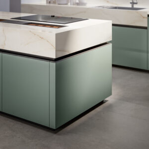 Modent kök med väggskåp i ljus grön nyans, blanklackade. Bänkskåp som är vita matt lackade, och bänkskiva i grå kompositsten