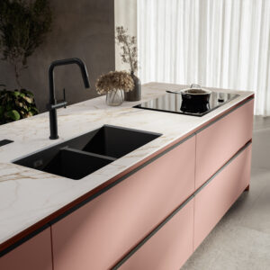 Modent kök med väggskåp i ljus rosa/aprikos nyans, blanklackade. Bänkskåp som är vita matt lackade, och bänkskiva i grå kompositsten